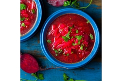 Bright red beetroot soup (borscht) served in blue bowls, garnished with fresh parsley